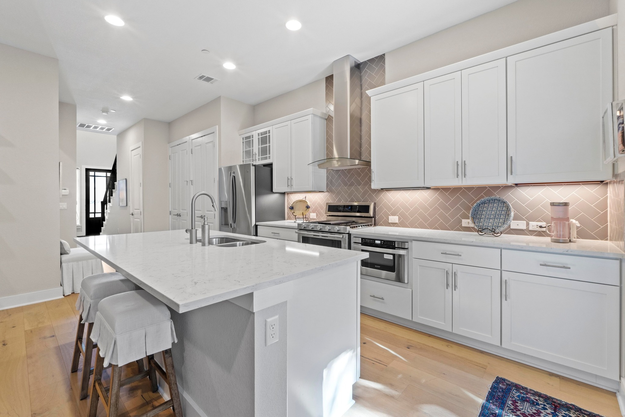 4323 Spicewood Springs Road, Unit 6 Austin, TX 78759 - Photo 14 of 40 Kitchen with appliances with stainless steel finishes, wall chimney exhaust hood, an island with sink, a breakfast bar area, and white cabinetry