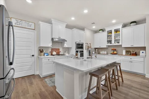 a kitchen with stainless steel appliances granite countertop a stove top oven a sink a refrigerator and white cabinets with wooden floor