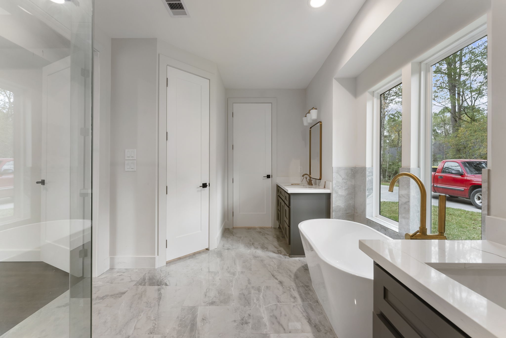 29001 Colin Court Waller, TX 77484 - Photo 21 of 47 Another view to show off the freestanding tub, picture windows offering plenty of natural light, a sleek vanity with a mirror, and a spacious glass shower. The light tile flooring and neutral walls create an airy and elegant atmosphere. This en-suite features two closets