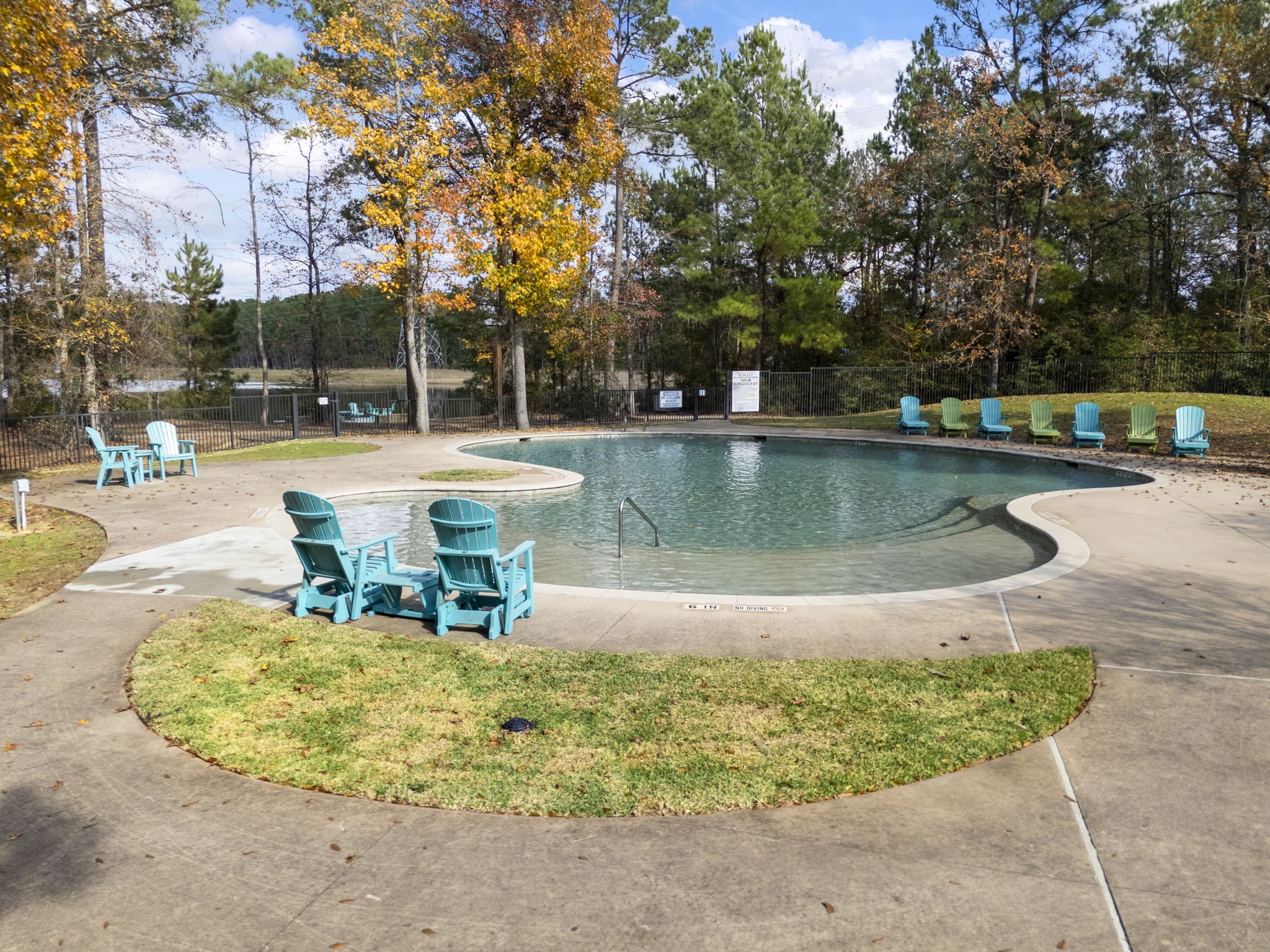 29001 Colin Court Waller, TX 77484 - Photo 41 of 47 Serene community outdoor pool surrounded by lush trees, with colorful Adirondack chairs for lounging. Perfect for relaxation and enjoying nature.
