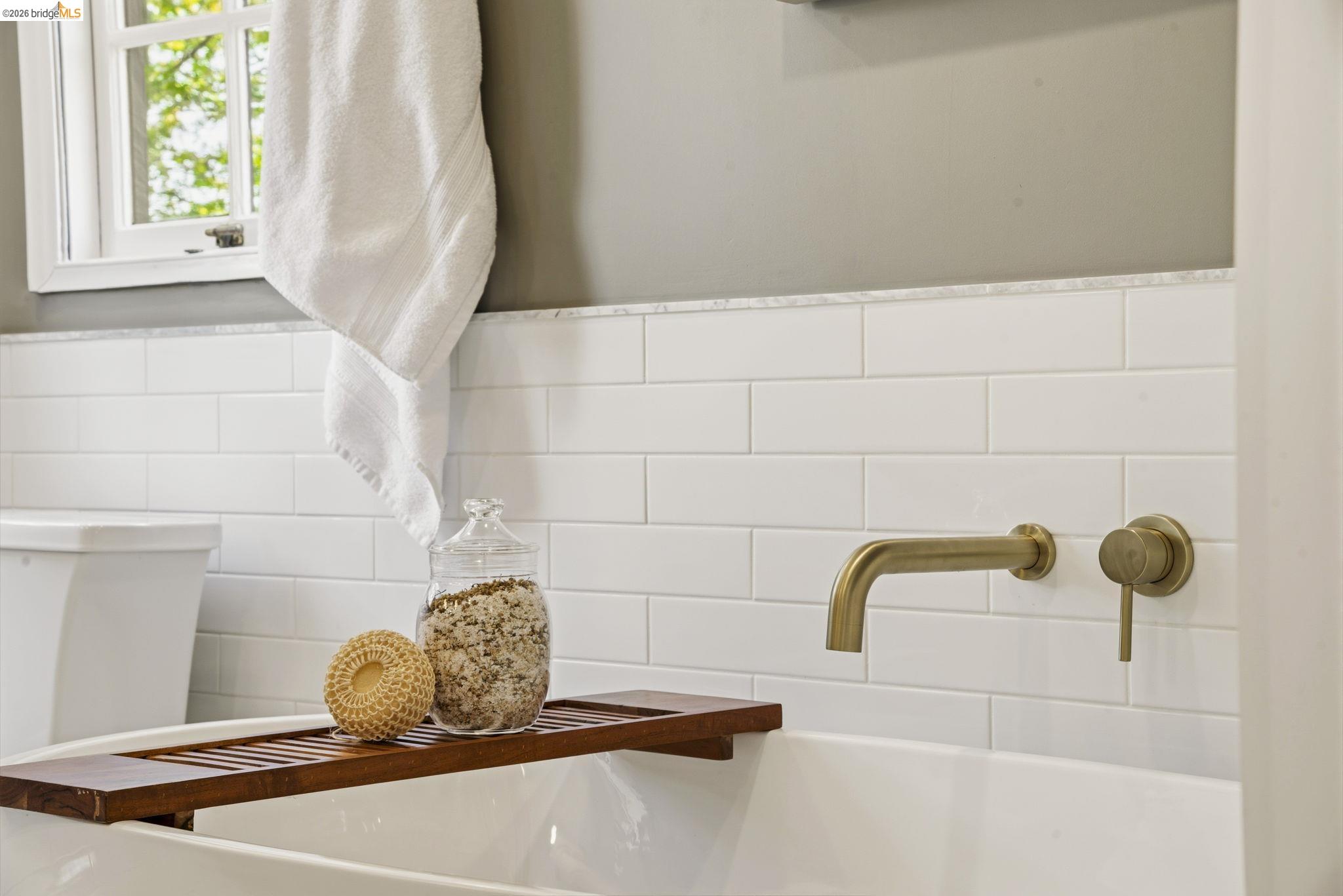 1087 Hubert Road Oakland, CA 94610 - Photo 24 of 67 Bathtub with a wall-mounted brass-finish faucet, white subway tile surround, and a coordinating marble-finish cap