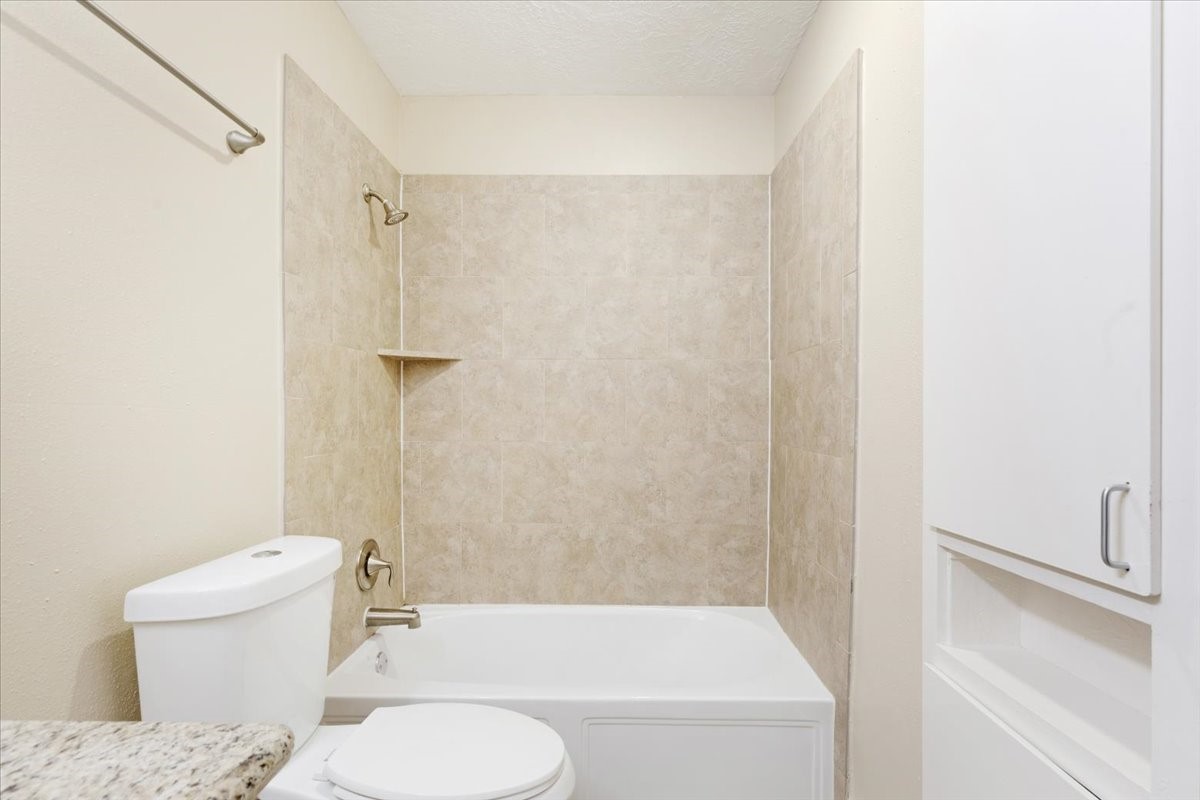 3502 Ocee Street, Unit 3502 Houston, TX 77063 - Photo 12 of 28 This bathroom features a clean design with a tiled shower and bathtub combo, modern fixtures, a white toilet, and built-in storage. It has a neutral color palette, giving it a fresh and inviting look.