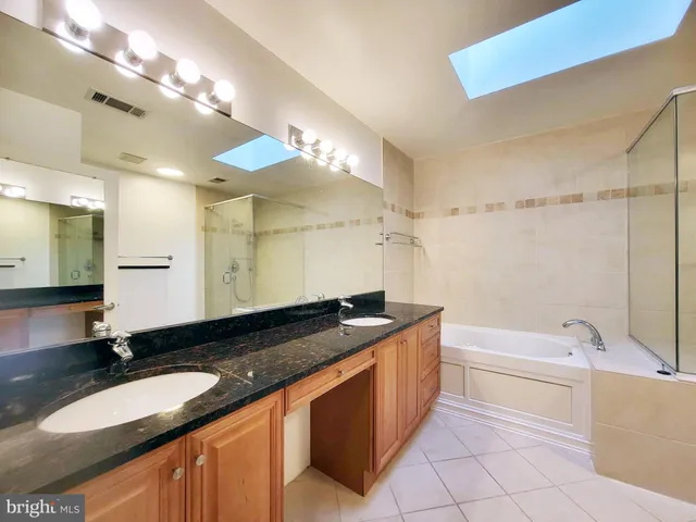 a bathroom with a granite countertop double vanity sink a mirror and a bathtub