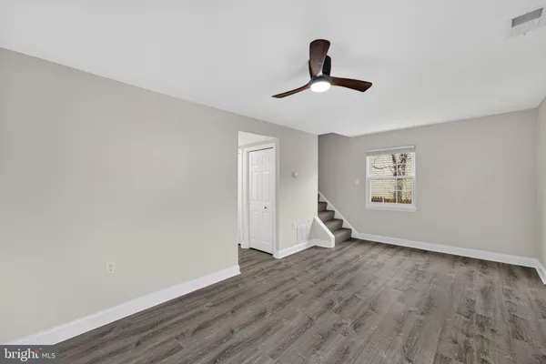 a view of an empty room with wooden floor and a ceiling fan