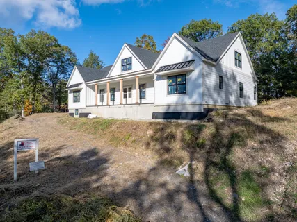 a view of a white house next to a yard with plants and large trees
