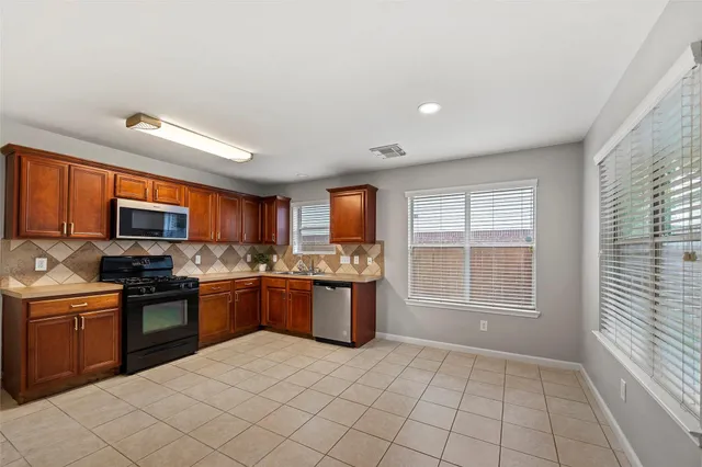 a kitchen with stainless steel appliances granite countertop a stove top oven a sink dishwasher a dining table and chairs with wooden floor