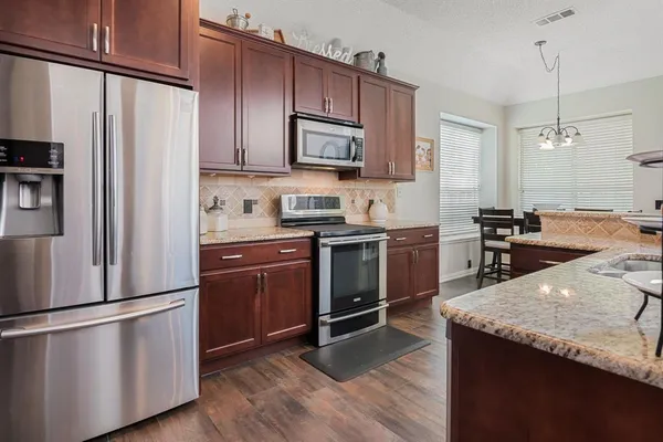 a kitchen with stainless steel appliances granite countertop a refrigerator a stove a sink dishwasher and a refrigerator with wooden floor