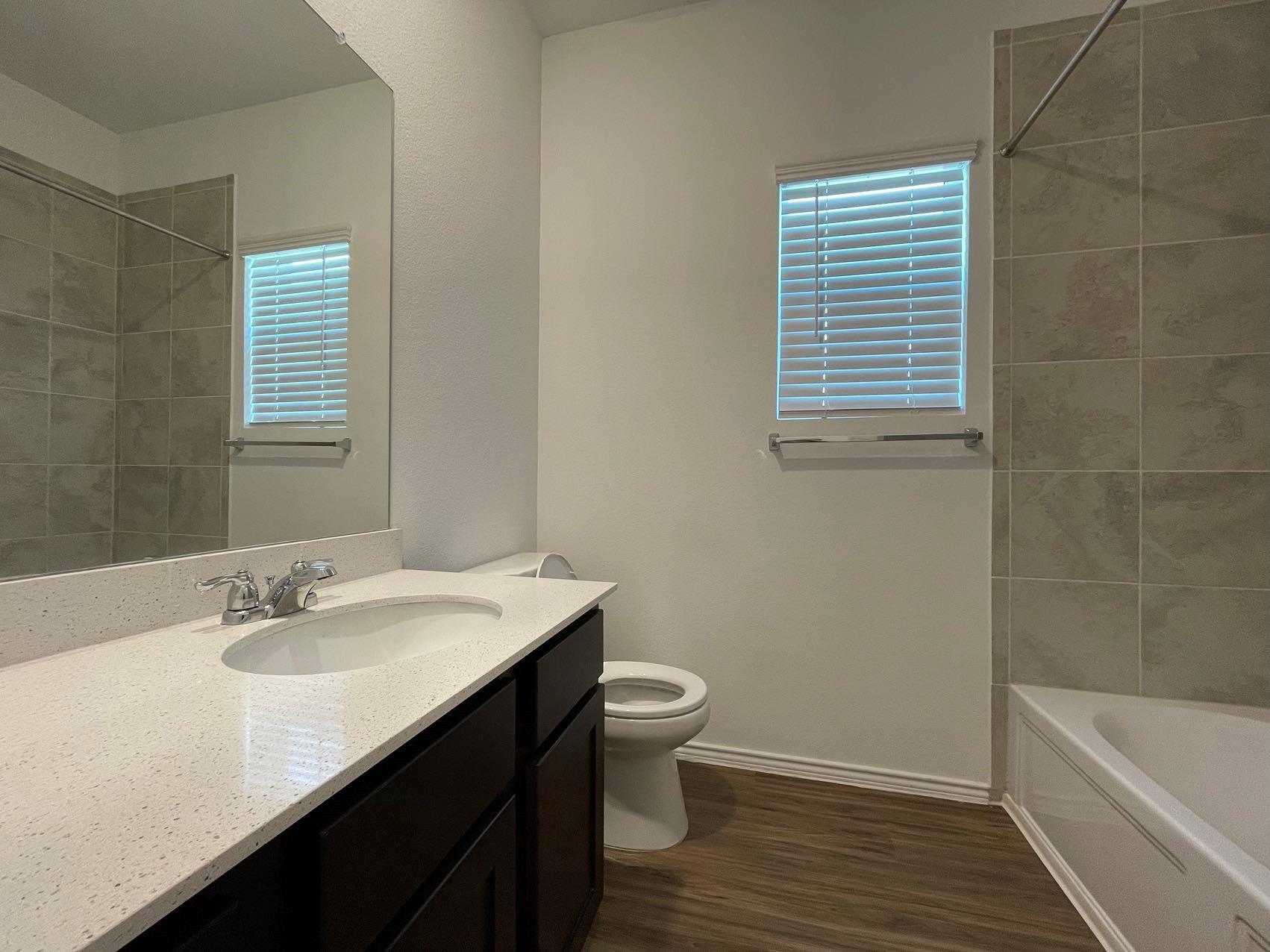 1625 Woolsey Way Leander, TX 78641 - Photo 9 of 17 Bathroom featuring a vanity with a white countertop and dark cabinetry, a built-in bathtub with tiled walls, and a window with blinds