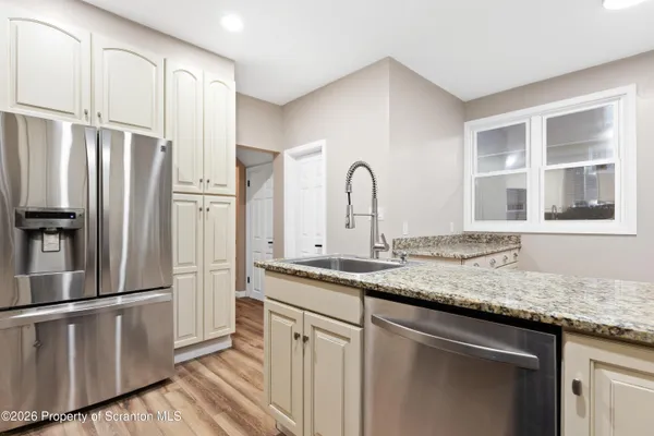 a kitchen with stainless steel appliances granite countertop a refrigerator a sink and white cabinets