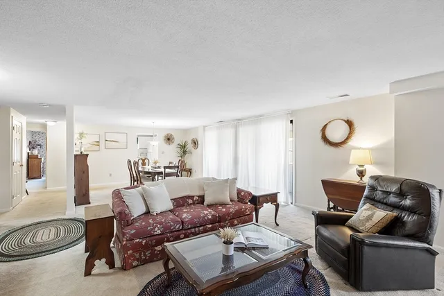 a view of a dining room and livingroom with furniture wooden floor a rug a painting and a chandelier