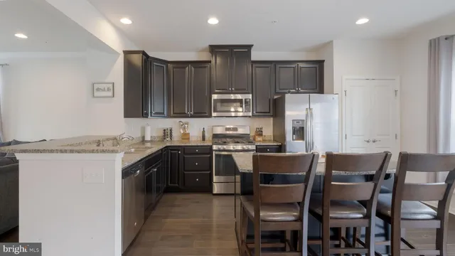 a kitchen with stainless steel appliances granite countertop a stove top oven a refrigerator a sink and chairs