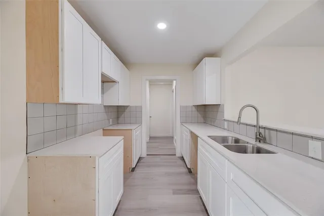 a kitchen with a sink dishwasher a stove top oven a refrigerator with white cabinets and wooden floor