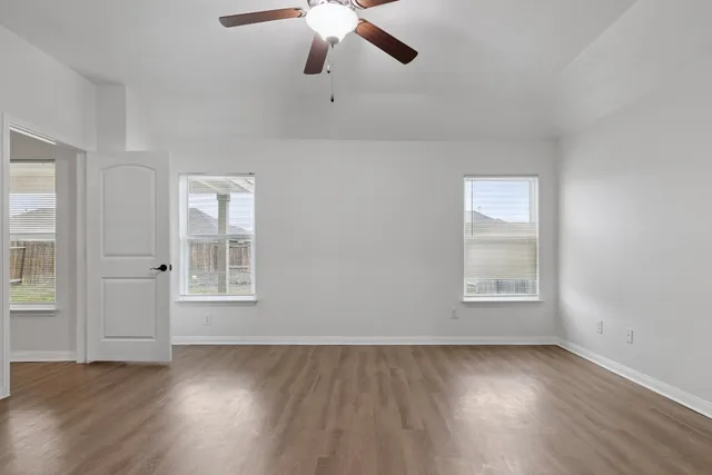 an empty room with wooden floor chandelier fan and windows