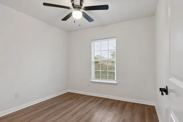 an empty room with wooden floor chandelier fan and windows