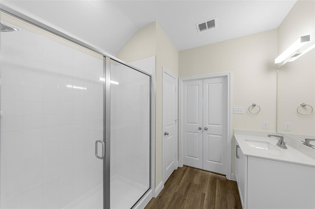 200 Pennington Road Josephine, TX 75173 - Photo 17 of 22 Contemporary bathroom featuring a glass-enclosed shower with white subway tile, a vanity with a white countertop and integrated sink, a large wall mirror, and wood-finish flooring