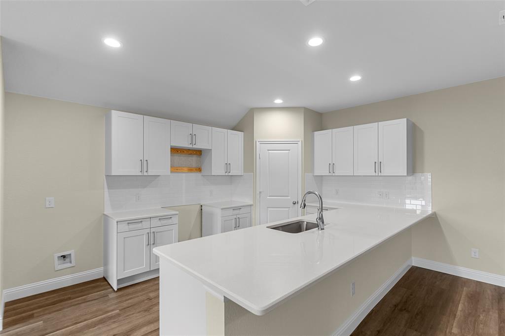 200 Pennington Road Josephine, TX 75173 - Photo 8 of 22 Modern kitchen featuring an island with an undermount sink and gooseneck faucet, white shaker-style cabinetry, white countertops, a subway tile backsplash, and wood-finish flooring