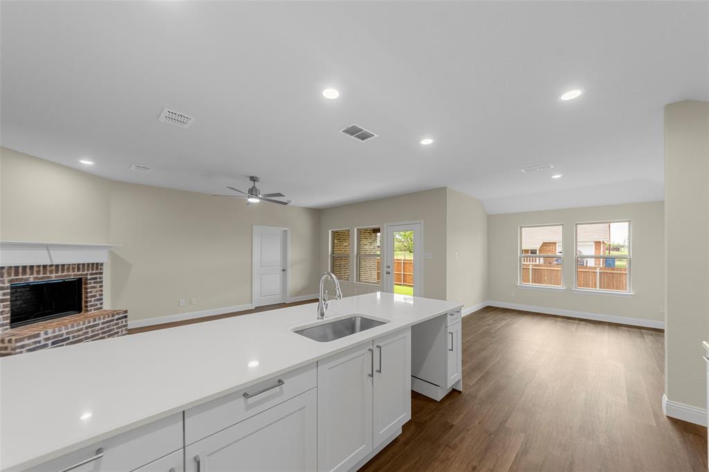 200 Pennington Road Josephine, TX 75173 - Photo 10 of 22 Expansive kitchen island with a built-in sink and white cabinetry, wood-finish flooring, recessed lighting, a brick fireplace with a white mantel, and multiple large windows