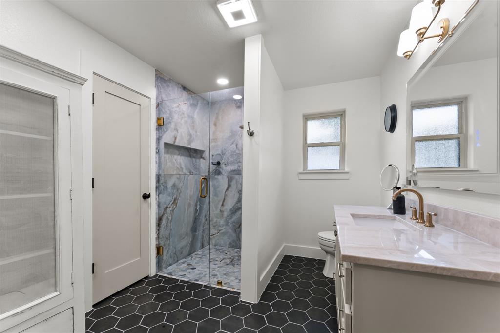 380 Farr Altom Road Seagoville, TX 75159 - Photo 17 of 30 Bathroom featuring a glass-enclosed shower with tiled walls and a built-in niche, black hexagonal floor tiling, a white vanity with a light-colored countertop and integrated sink, a gold-toned faucet, and a large mirror with an overhead light fixture