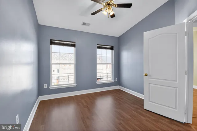 an empty room with wooden floor chandelier fan and windows