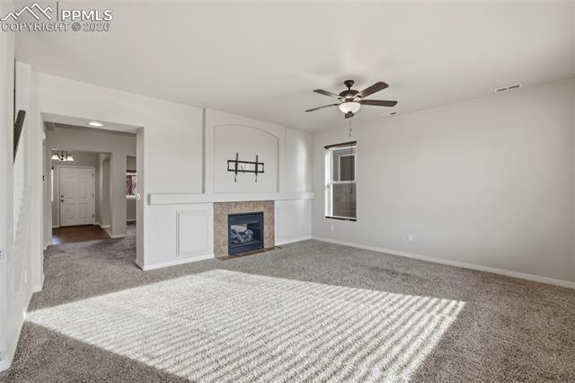 2224 Reed Grass Way Colorado Springs, CO 80915 - Photo 10 of 39 Unfurnished living room with a tiled fireplace, carpet flooring, and a ceiling fan