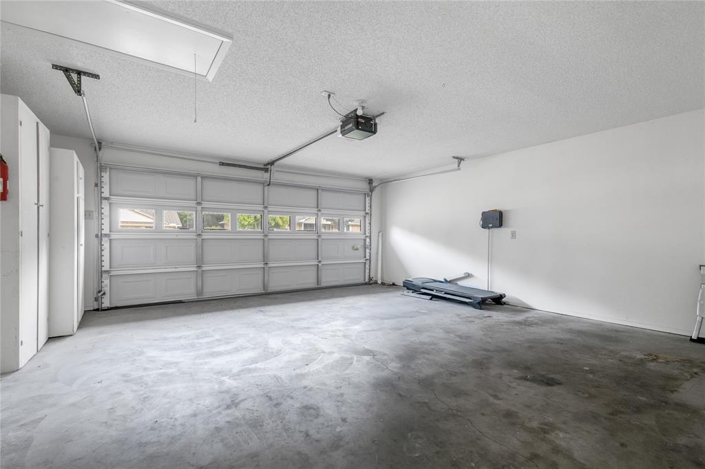 1609 Robin Street Mineola, TX 75773 - Photo 22 of 24 Spacious garage featuring a sectional garage door with multiple windows, an automatic opener, built-in storage cabinets, and a pull-down attic access ladder