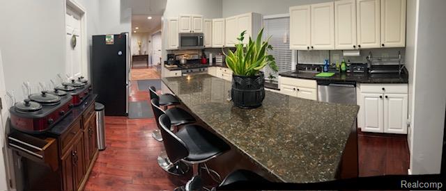 89 Muir Road Grosse Pointe, MI 48236 - Photo 15 of 29 Kitchen featuring an expansive island with a dark speckled countertop, wood-finish flooring, white cabinetry, and stainless steel appliances