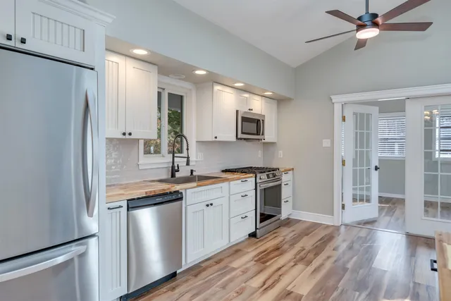 a kitchen with stainless steel appliances granite countertop a refrigerator a stove a sink and white cabinets with wooden floor