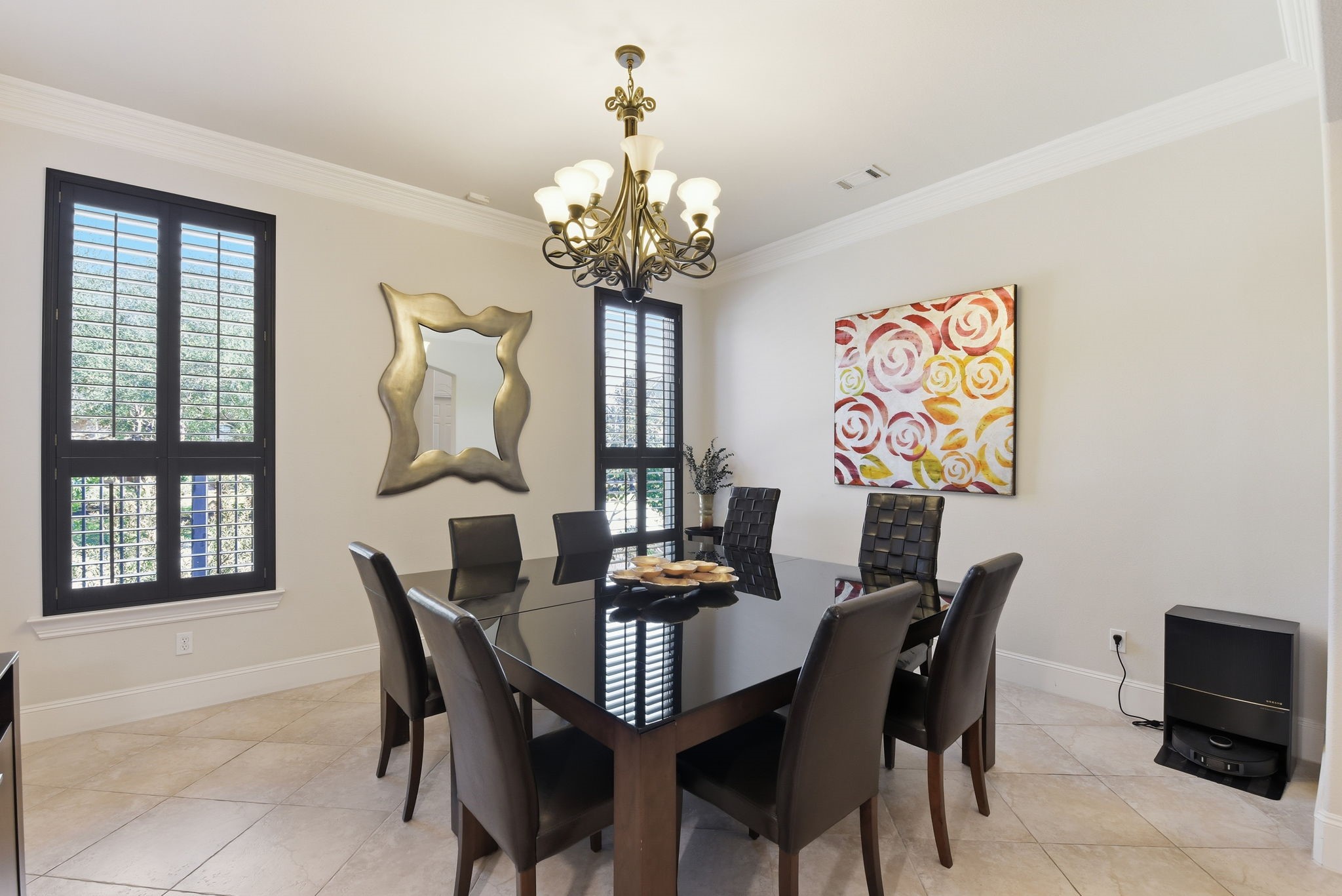 223 South Bauer Point Circle Spring, TX 77389 - Photo 12 of 50 This dining room features a modern design with a large glass table and eight leather chairs. It has tiled flooring, a stylish chandelier, and natural light from windows with shutters. The walls are adorned with contemporary art and a decorative mirror.