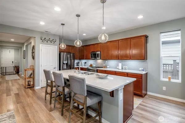 a kitchen with stainless steel appliances granite countertop a stove a refrigerator a kitchen island a dining table and chairs with wooden floor