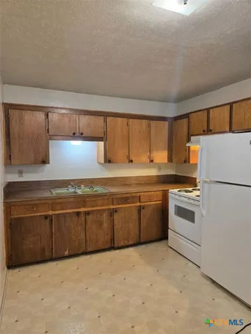 a kitchen with granite countertop a refrigerator a sink and white cabinets