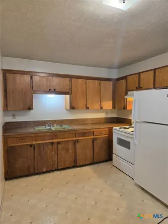 a kitchen with granite countertop a refrigerator a sink and white cabinets