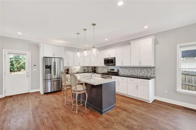 a kitchen with stainless steel appliances a stove a sink dishwasher a refrigerator and white cabinets with wooden floor