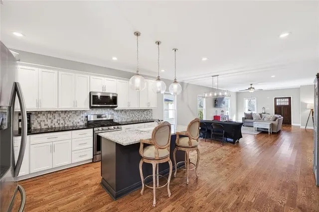 a kitchen with stainless steel appliances kitchen island granite countertop a stove a sink a refrigerator and white cabinets with wooden floor