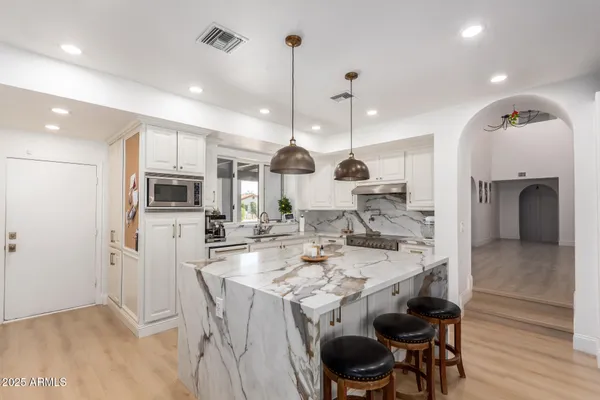 a kitchen with stainless steel appliances granite countertop a stove a sink a refrigerator and a dining table with white cabinets