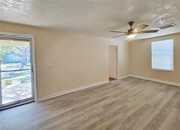 an empty room with wooden floor chandelier fan and windows