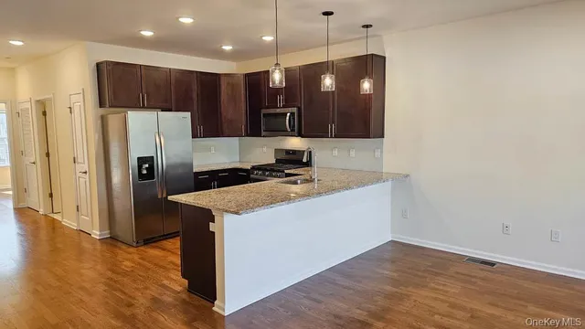 a kitchen with stainless steel appliances granite countertop a refrigerator a sink a stove and a wooden floors