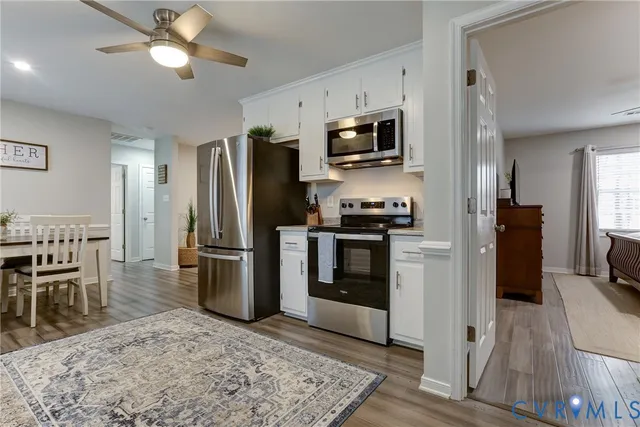 a kitchen with stainless steel appliances kitchen island granite countertop a refrigerator a stove a sink a dining table and chairs with wooden floor