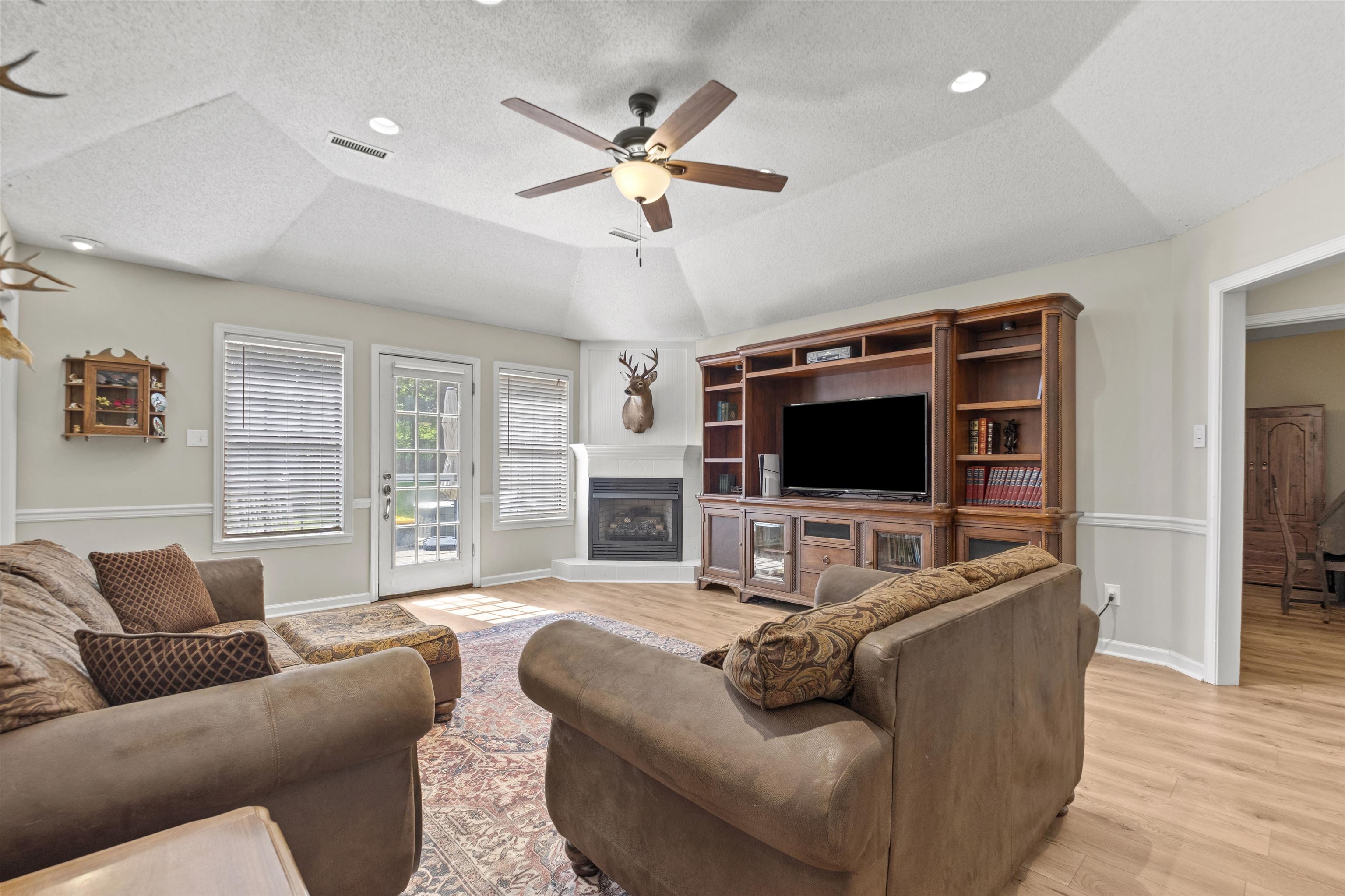 3601 Marshall Road Munford, TN 38058 - Photo 18 of 35 Living area with vaulted ceiling, wood-finish flooring, corner fireplace with white mantel, built-in entertainment center, and exterior access via a glass-paneled door