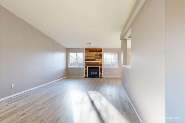an empty room with wooden floor fireplace and windows