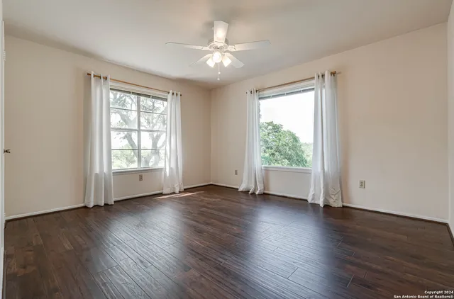 an empty room with wooden floor chandelier fan and windows