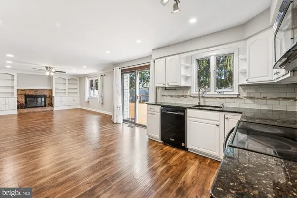 a large kitchen with granite countertop a stove top oven a sink and white cabinets with wooden floor