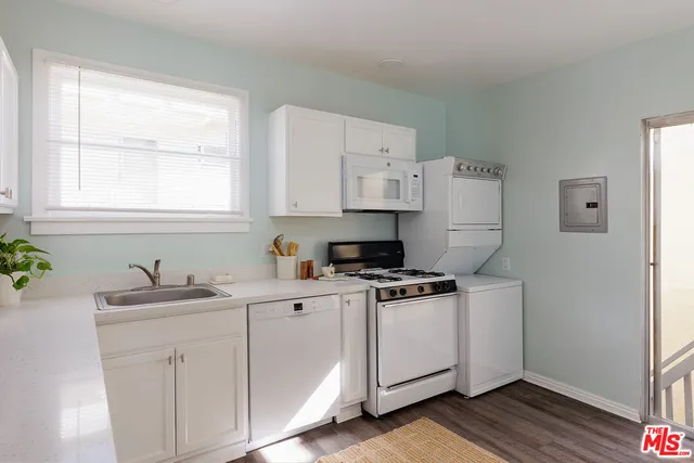a kitchen with stainless steel appliances white cabinets a sink a stove a window and wooden floor