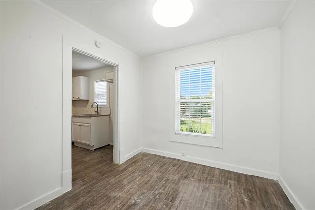 a view of a kitchen and an empty room with wooden floor and a window