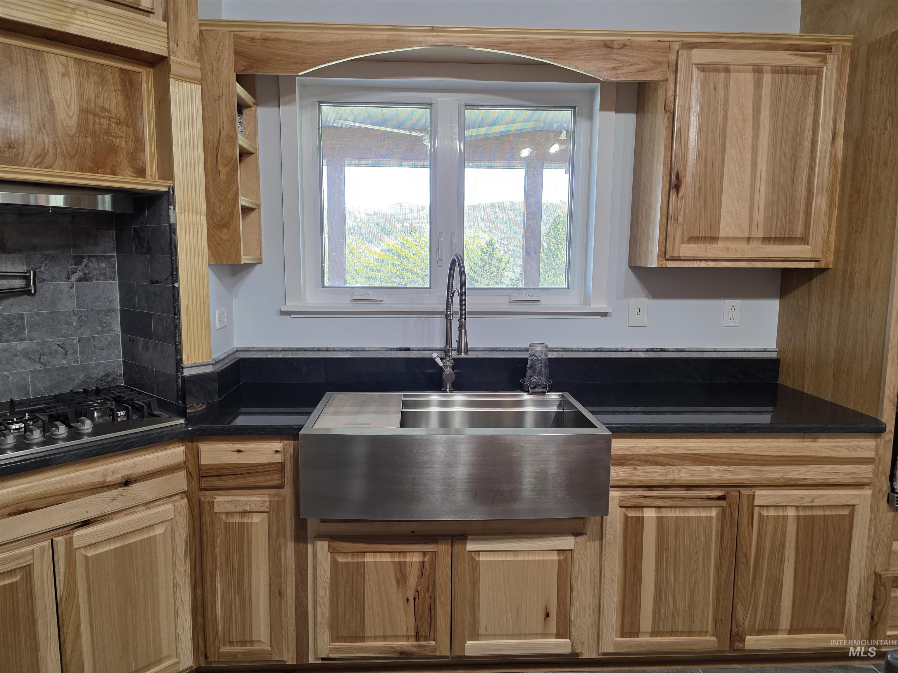 107 Pine Road Kamiah, ID 83536 - Photo 11 of 41 Kitchen featuring natural wood cabinetry, a stainless steel apron front sink, dark countertops, and a gray tile backsplash surrounding the gas range