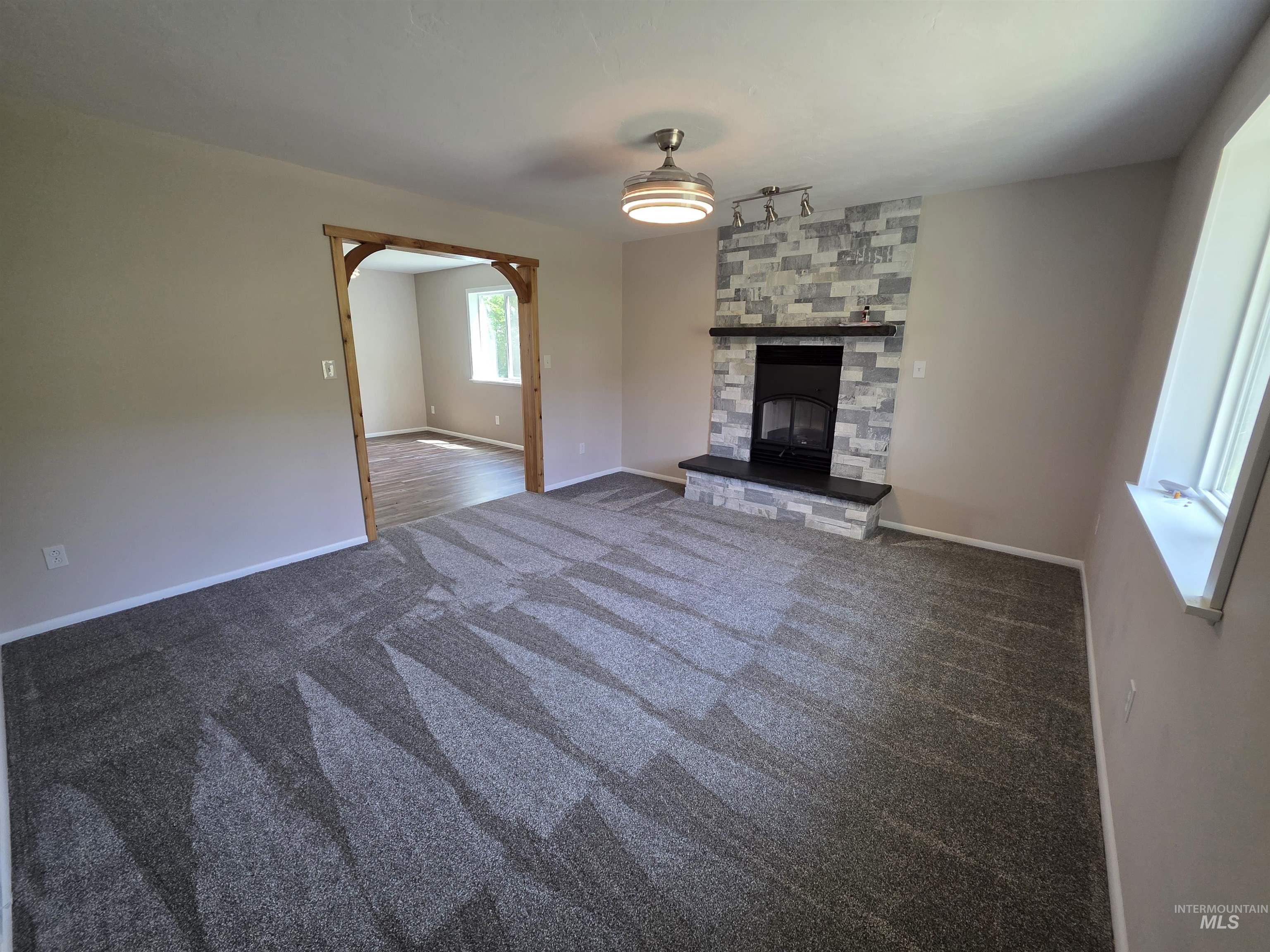107 Pine Road Kamiah, ID 83536 - Photo 14 of 41 Living area featuring a modern fireplace with stone-look tile surround and black hearth, patterned carpet flooring, and a wood-framed archway opening to an additional room with wood-finish flooring