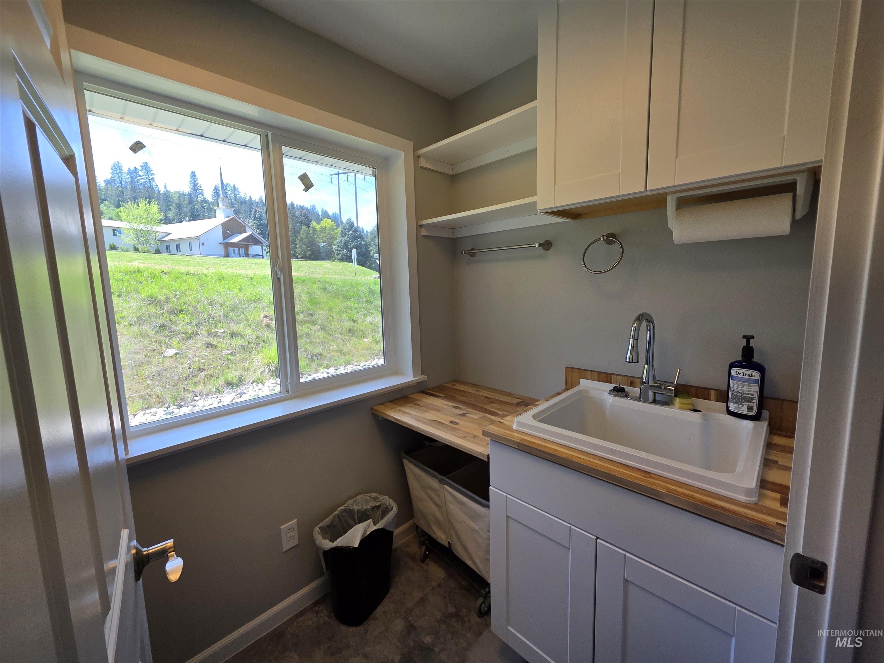 107 Pine Road Kamiah, ID 83536 - Photo 17 of 41 Utility sink with wood-finish countertop, white cabinetry, and overhead shelving