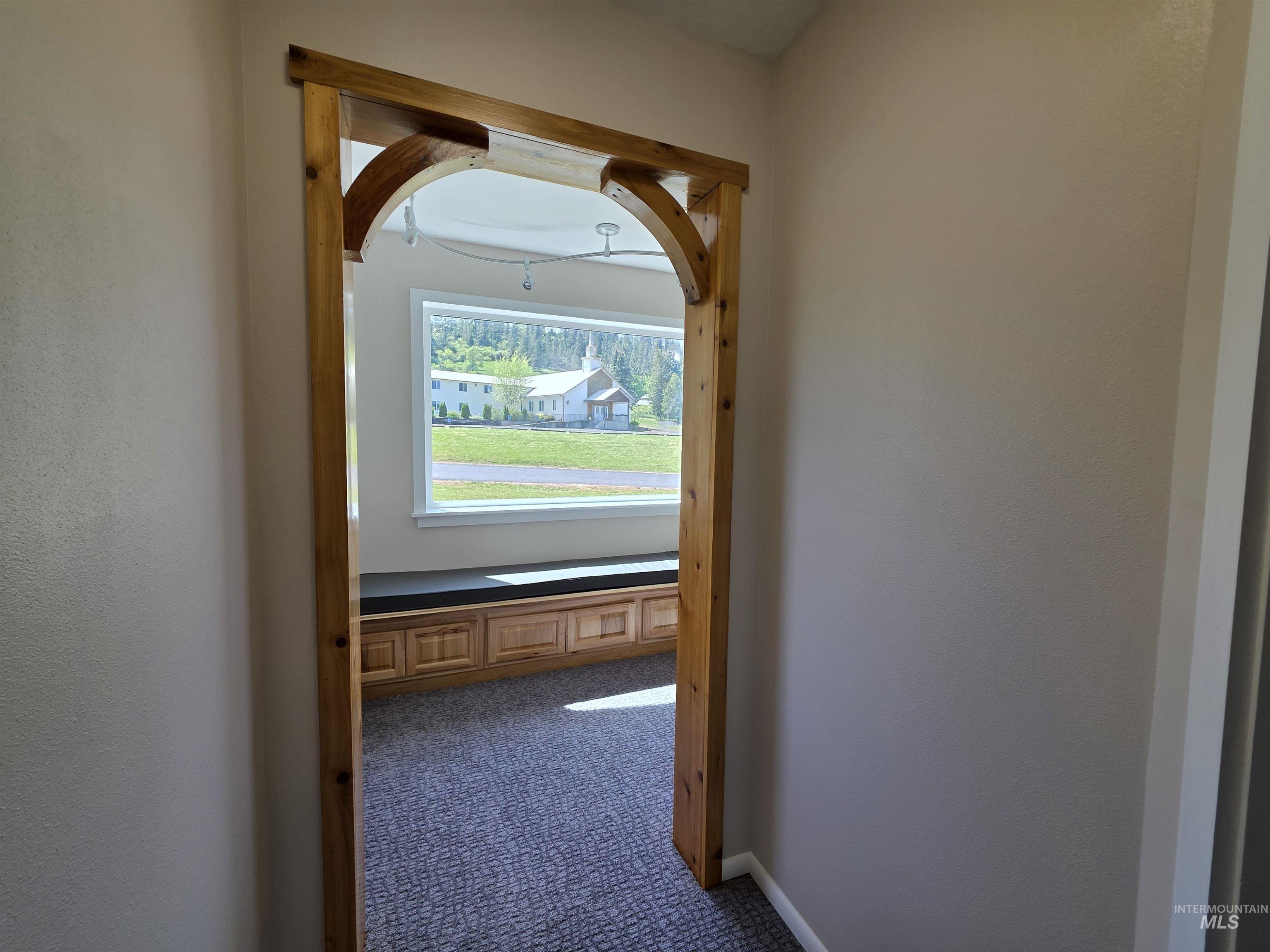 107 Pine Road Kamiah, ID 83536 - Photo 30 of 41 Wood-finish arched doorway opening into a room featuring a wide window, built-in cabinetry, and gray patterned carpet