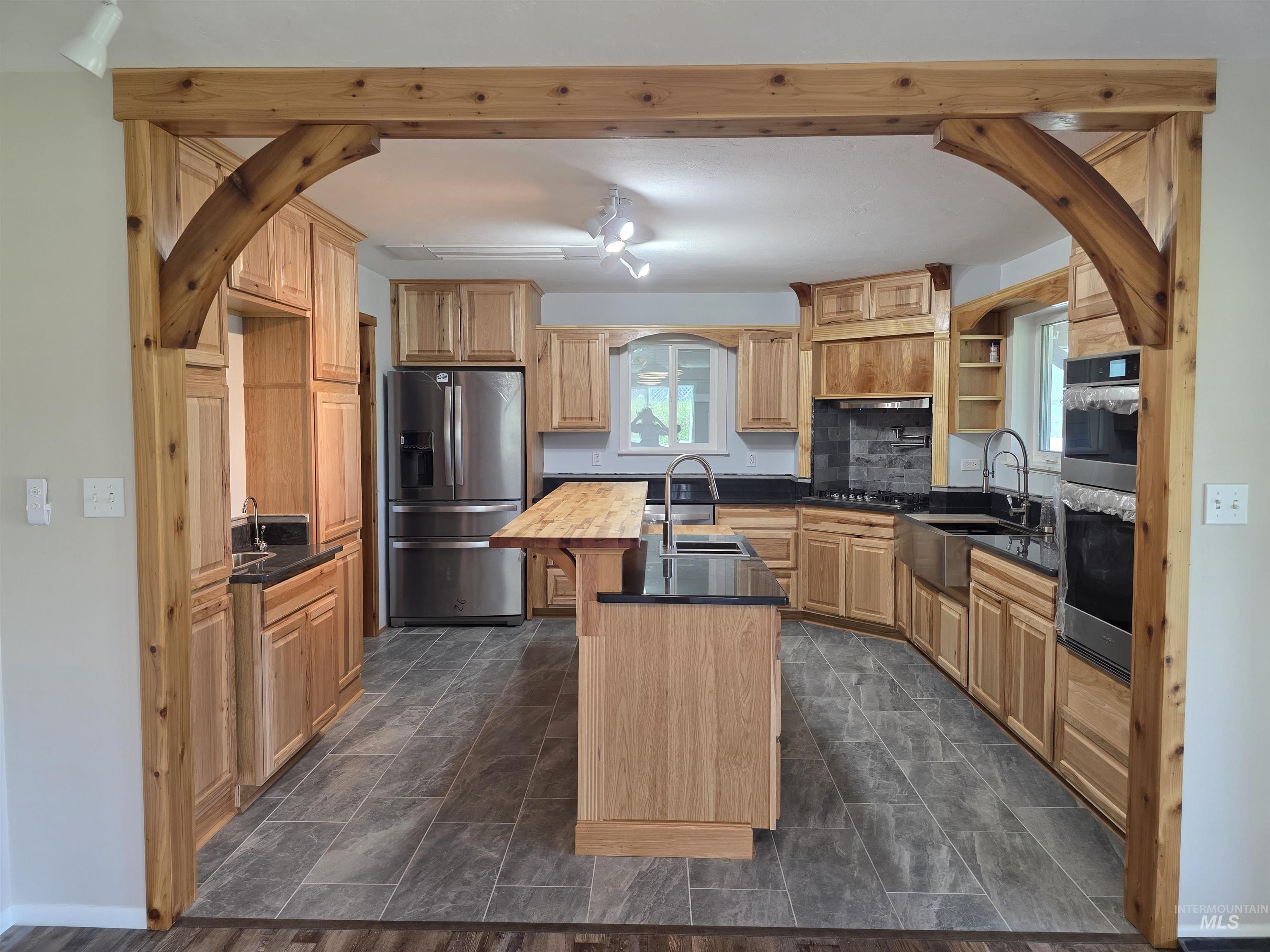 107 Pine Road Kamiah, ID 83536 - Photo 7 of 41 Spacious kitchen featuring an arched wood beam entryway, shaker-style wood cabinetry, dark countertops, a central island with wood-finish countertop, and stainless steel appliances