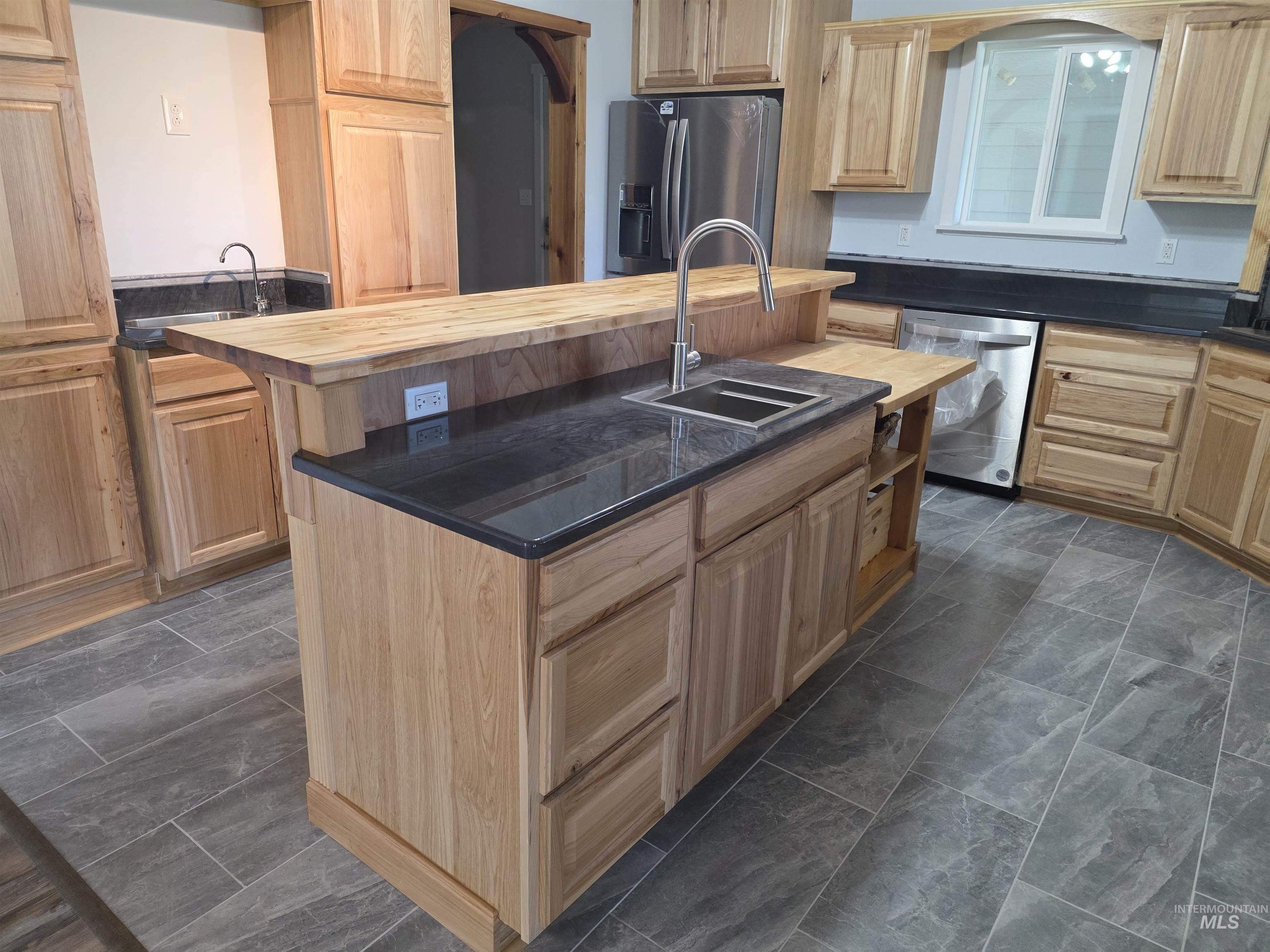 107 Pine Road Kamiah, ID 83536 - Photo 8 of 41 Central kitchen island featuring a double-basin stainless steel sink with a high-arc faucet, dark stone countertops, and light wood cabinetry