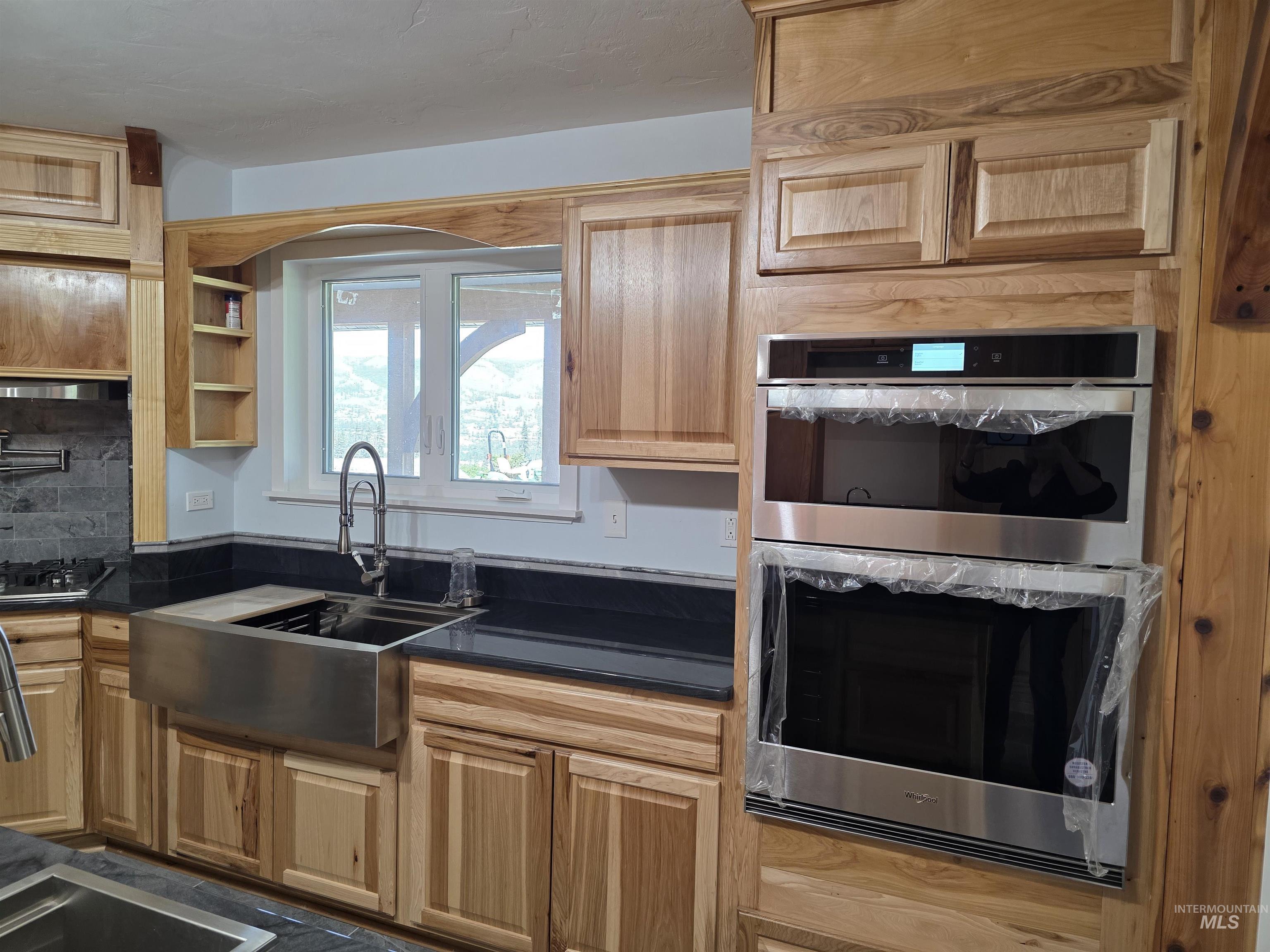 107 Pine Road Kamiah, ID 83536 - Photo 10 of 41 Kitchen featuring light wood cabinetry, a stainless steel farmhouse sink with a gooseneck faucet, black countertops, and built-in stainless steel double ovens